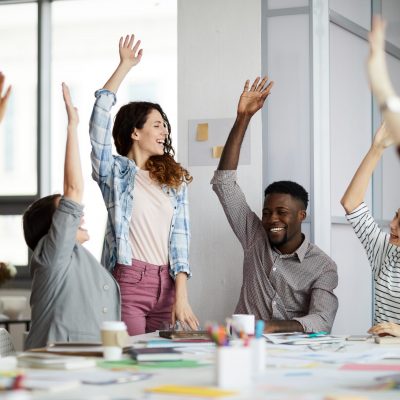 Multi-ethnic team of young businesspeople  raising hands celebrating success in office, copy space
